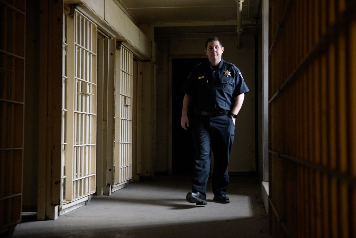 A correctional officer walks through a dimly lit hallway lined with jail cells.