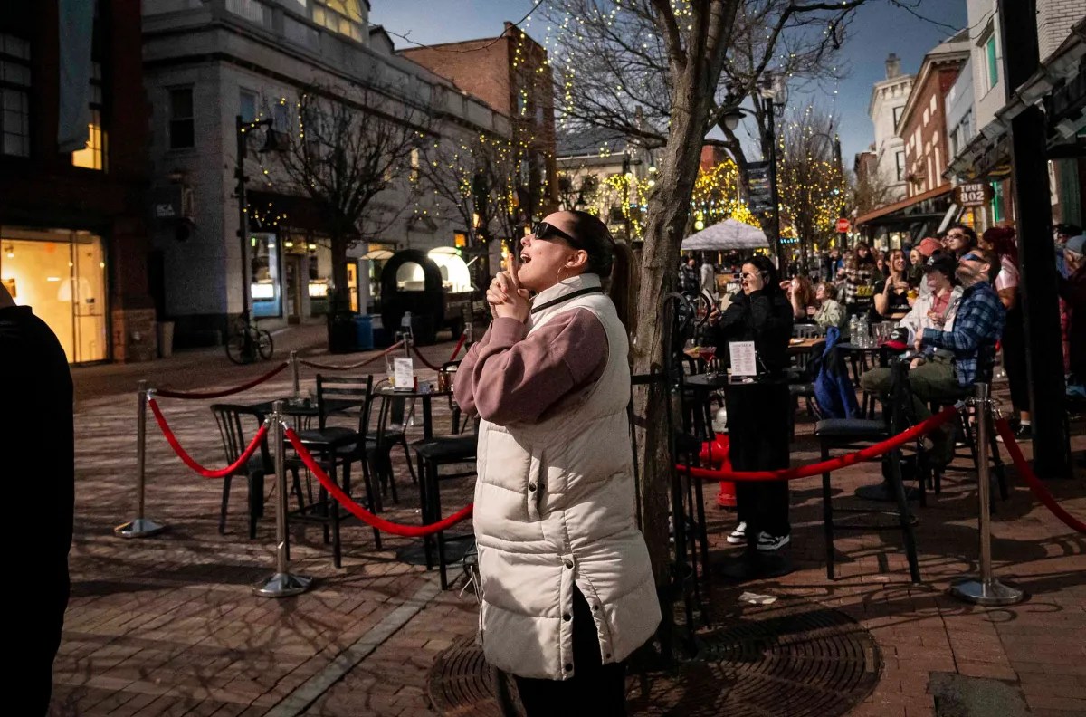 Person looking up in apparent awe or surprise at an outdoor evening event with onlookers in the background.