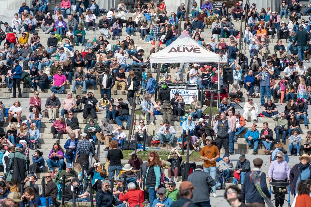 Crowd of people sitting and standing on outdoor steps at a public event.