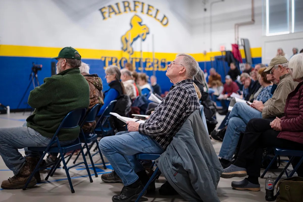 A group of people sitting in chairs, attentively watching a presentation in a gymnasium with a "Fairfield Trotters" logo on the wall.