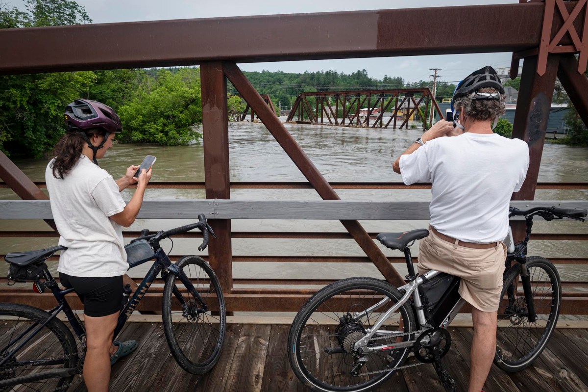 two people standing on a bridge with their bicycles.