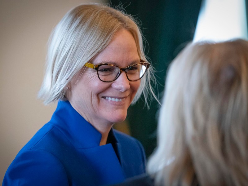 Woman in blue blazer and glasses smiling during a conversation.
