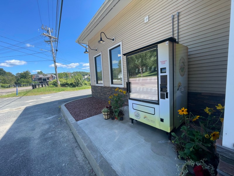 Refrigerated vending machine outside a building on a sunny day, offering farm-fresh products.