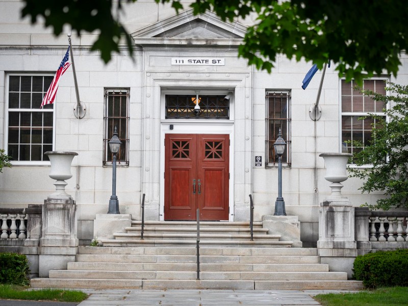 A beige stone building with a prominent entrance featuring double wooden doors, two lanterns, and a staircase. The building is located at 111 State Street and has American and state flags displayed.