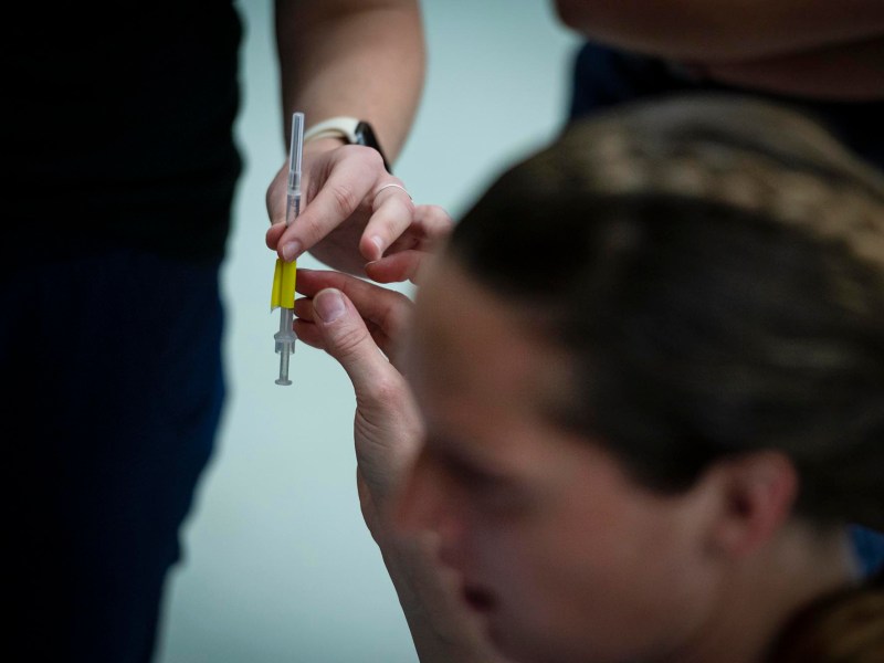 Hands preparing a syringe while a person's blurred face is visible in the foreground.