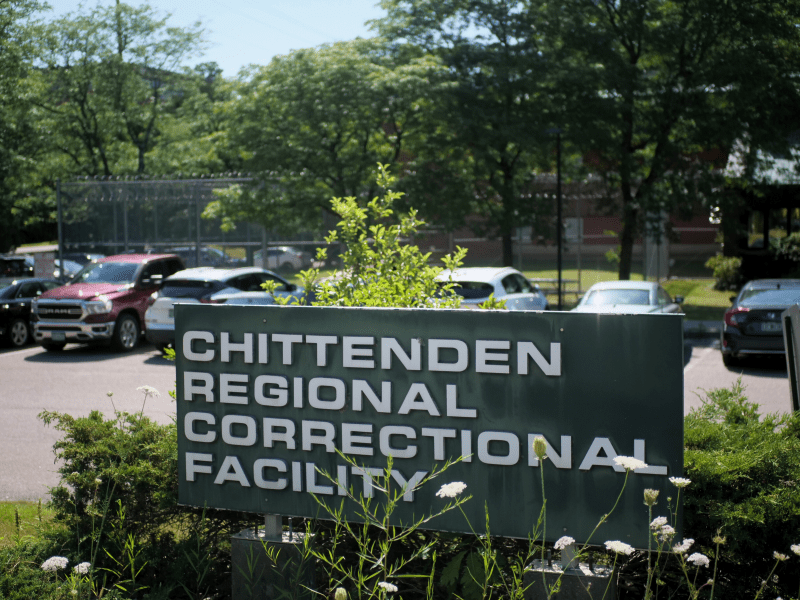 A green sign reads "Chittenden Regional Correctional Facility" with parked cars and a fence visible in the background.